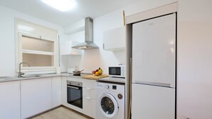 A modern kitchen with white cabinets, a built-in oven, a microwave, a washing machine, and a refrigerator.