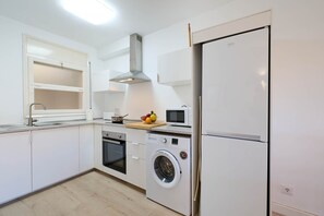 A modern kitchen with white cabinets, a built-in oven, a microwave, a washing machine, and a refrigerator.