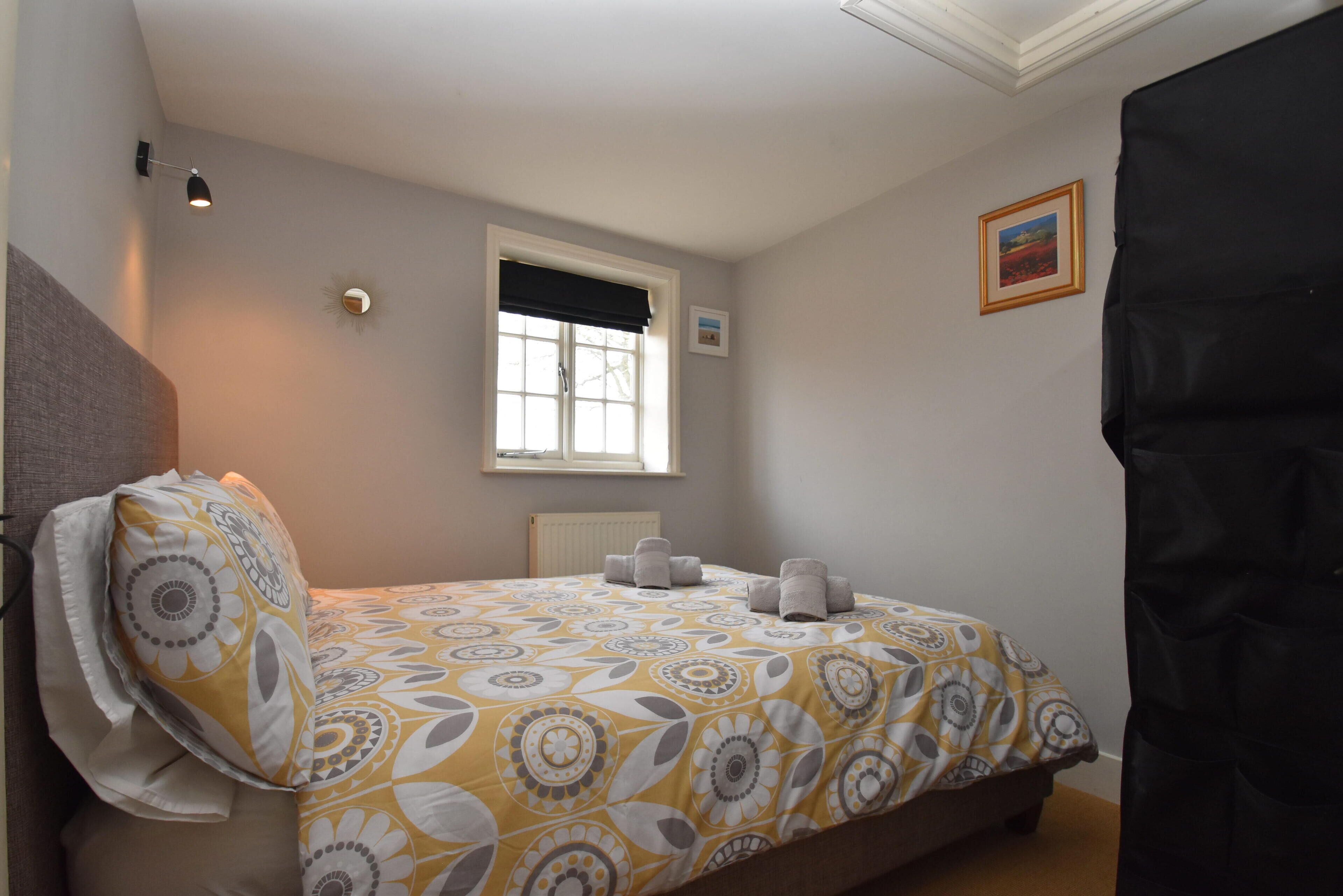 Ein Schlafzimmer mit Bett, Fenster, Heizkörper und einer Wandleuchte.