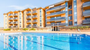 Ein modernes Hotel mit mehreren Balkonen, einem Schwimmbad und blauem Himmel.