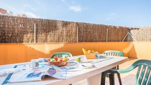 Ein Esstisch mit einer Zeitung, einer Obstschale und einem Brotkorb auf einer Terrasses mit orangefarbenen Wänden und einem Holzzaun im Hintergrund.
