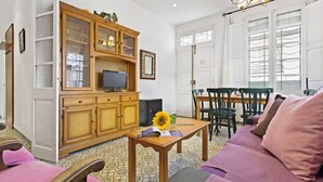 A living room with a wooden cabinet, a television, a dining table with chairs, and a sofa with cushions.