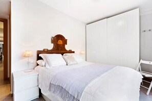 A neatly arranged bedroom with a wooden headboard, two bedside lamps, a white bedspread, and a white chair.
