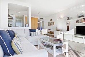 Un salon moderne avec un canapé blanc, une table basse en verre et un téléviseur à écran plat.