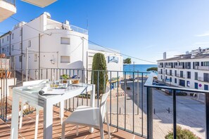 A balcony with a table and chairs, overlooking a street with buildings and a clear blue sky.