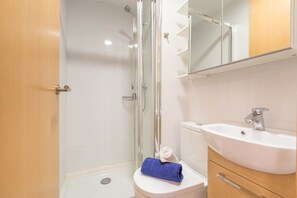 A bathroom with a glass shower enclosure, a white sink, and a wooden cabinet.