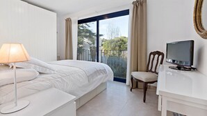 A bedroom with a bed, a desk with a television, a chair, and a window with curtains.