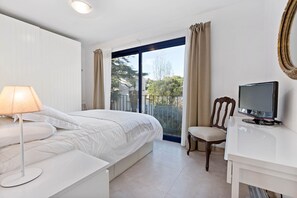 Une chambre à coucher avec un lit, un bureau avec une télévision, une chaise et une fenêtre avec des rideaux.