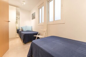 A hotel room with two beds, a chair, and a window.