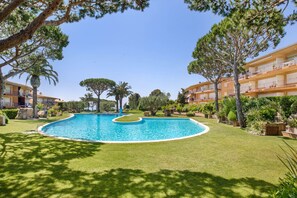 A swimming pool surrounded by well-maintained grass and trees, with a building in the background.