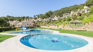 Una piscina de diseño curvo, rodeada por un sendero pavimentado. Al fondo, edificios en la ladera con un estilo arquitectónico uniforme.