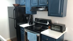 A compact kitchen with dark blue cabinets, a black refrigerator, a stove, a coffee maker, and a toaster. - Quiet townhome between Canandaigua and Naples in the Finger Lakes (Canandaigua)