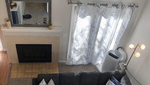 A living room with a black sofa, two patterned cushions, a wooden coffee table, a fireplace, a ceiling-mounted air purifier, and a floor lamp. - Quiet townhome between Canandaigua and Naples in the Finger Lakes (Canandaigua)