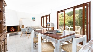 A cozy living room with a fireplace, a dining area with a wooden table and chairs, and a balcony with outdoor furniture.