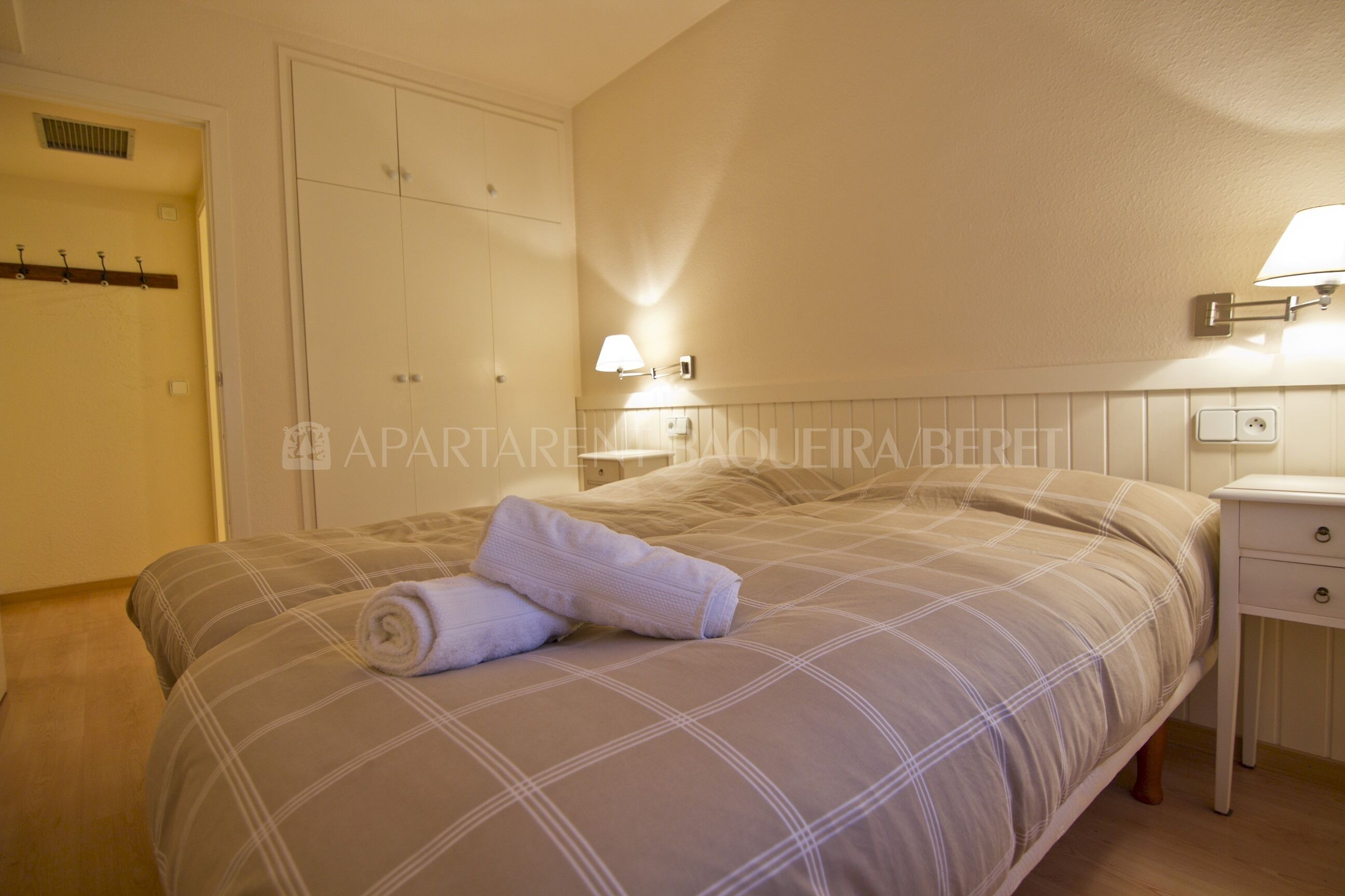 Een slaapkamer met een bed, nachtkastje, lamp en kledingkast.