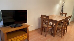 Un comedor con una mesa y sillas de madera, un televisor sobre un mueble de madera y una lámpara.