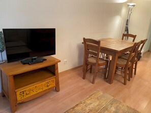Zona pranzo con tavolo e sedie in legno, televisore su un mobile in legno e una lampada.
