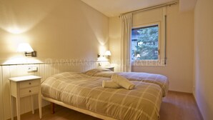 Un dormitorio con dos camas, una mesita de noche, una lámpara y una ventana con cortinas.