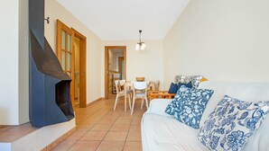Una sala de estar con chimenea, un sofá con cojines estampados, una zona de comedor con mesa y sillas, y un pasillo con una puerta.