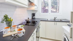 A modern kitchen with white cabinets, a black countertop, a built-in stove, and a window with a view of trees. - 1CAR PL - Basic apartment with communal pool near Llafranc beach (Llafranc)