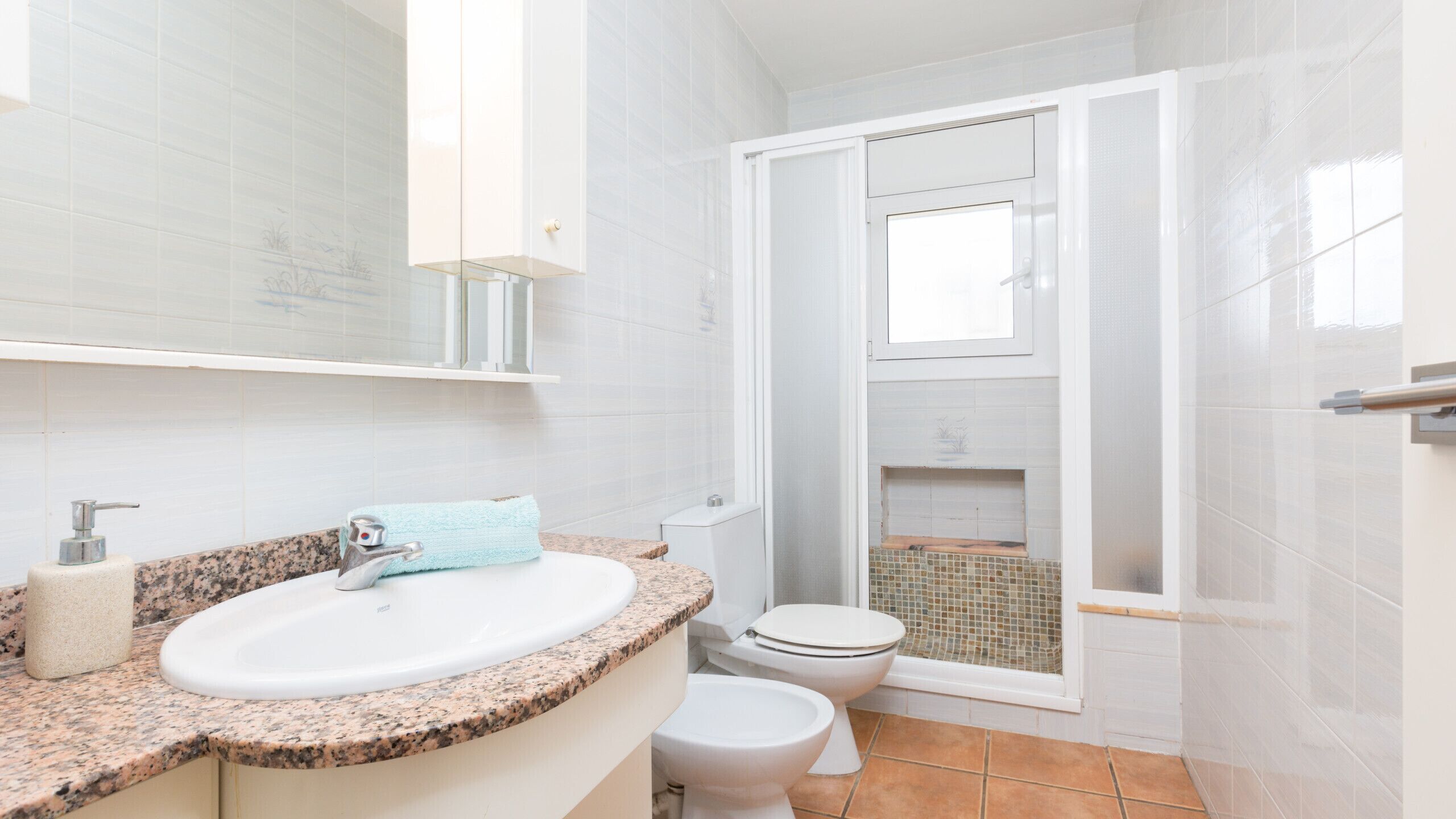 Baño con lavamanos de encimera de granito, inodoro y zona de ducha.
