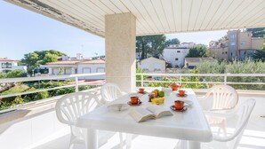 A sunlit outdoor dining area with a table set for two, surrounded by white chairs, overlooking a residential neighborhood. - 1OP 01 - Apartment located in Pals, in a residential complex with swimming pool, 400 m from the beach (Pals)