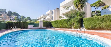 Una piscina con agua azul cristalina, rodeada de edificios modernos y vegetación.