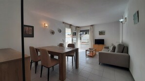 A living room with a sofa, a TV, and a dining area with chairs and a table. - 1OP 01 - Apartment located in Pals, in a residential complex with swimming pool, 400 m from the beach (Pals)