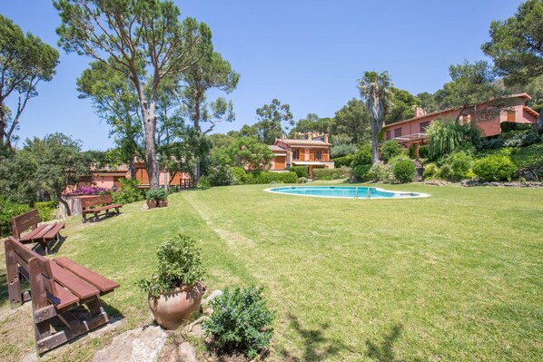 Une pelouse bien entretenue, agrémentée d’une piscine, de bancs en bois et d’une maison avec un toit en tuiles.