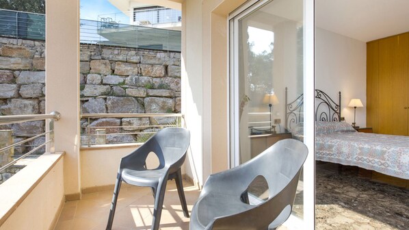 A balcony with stone walls, a bed with a patterned bedspread, and a chair.