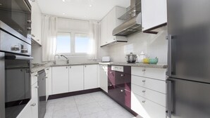 Une cuisine moderne avec des meubles blancs, des appareils en acier inoxydable et une fenêtre agrémentée de rideaux blancs.