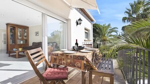 Une terrasse avec une table dressée pour le repas, une chaise rembourrée et une vue sur une maison et des palmiers.