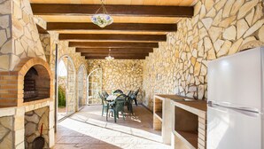 Un espace de restauration extérieur avec des murs en pierre, un four en briques, des poutres en bois et un luminaire suspendu.