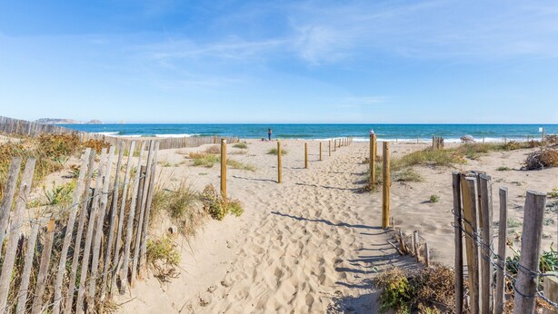 Un sentier de sable bordé de poteaux en bois et d’une clôture, qui mène à l’océan.