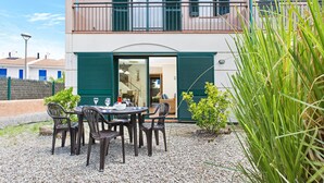 Un bâtiment à deux étages doté d’un balcon, d’un espace extérieur aménagé avec des chaises et une table, et d’un sol recouvert de gravier.