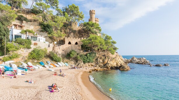 A beach with a castle on a cliff, boats, and people relaxing. - 2SEN01 - House with private pool located in a quiet area just 2.5 km from the beautiful beach of Canyelles (Lloret de Mar)