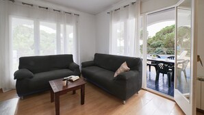 A living room with two dark sofas, a wooden coffee table, and a sliding glass door leading to an outdoor patio with a table and chairs. - 2SEN01 - House with private pool located in a quiet area just 2.5 km from the beautiful beach of Canyelles (Lloret de Mar)