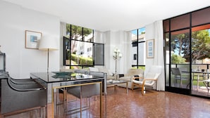 A modern living room with a glass dining table, a sofa, and a chair. There is a large window with a view of the outside. - 1PINEDA 01 - Cozy apartment for 8 persons  situated a few minutes walk from the beach of  Calella de Palafrugell (Calella de Palafrugell)