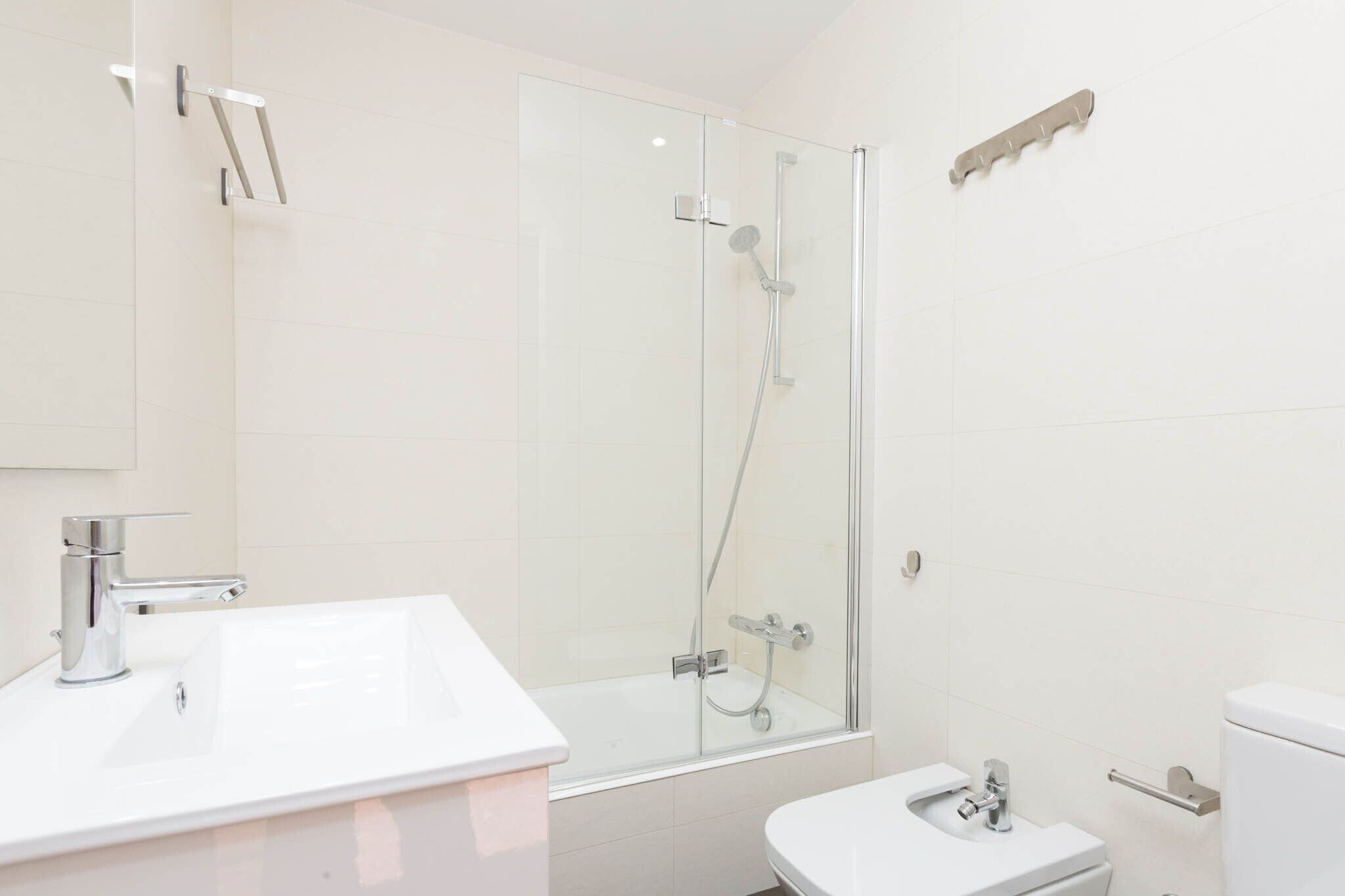 Un bany modern amb dutxa envidriada, un lavabo blanc i un vàter.