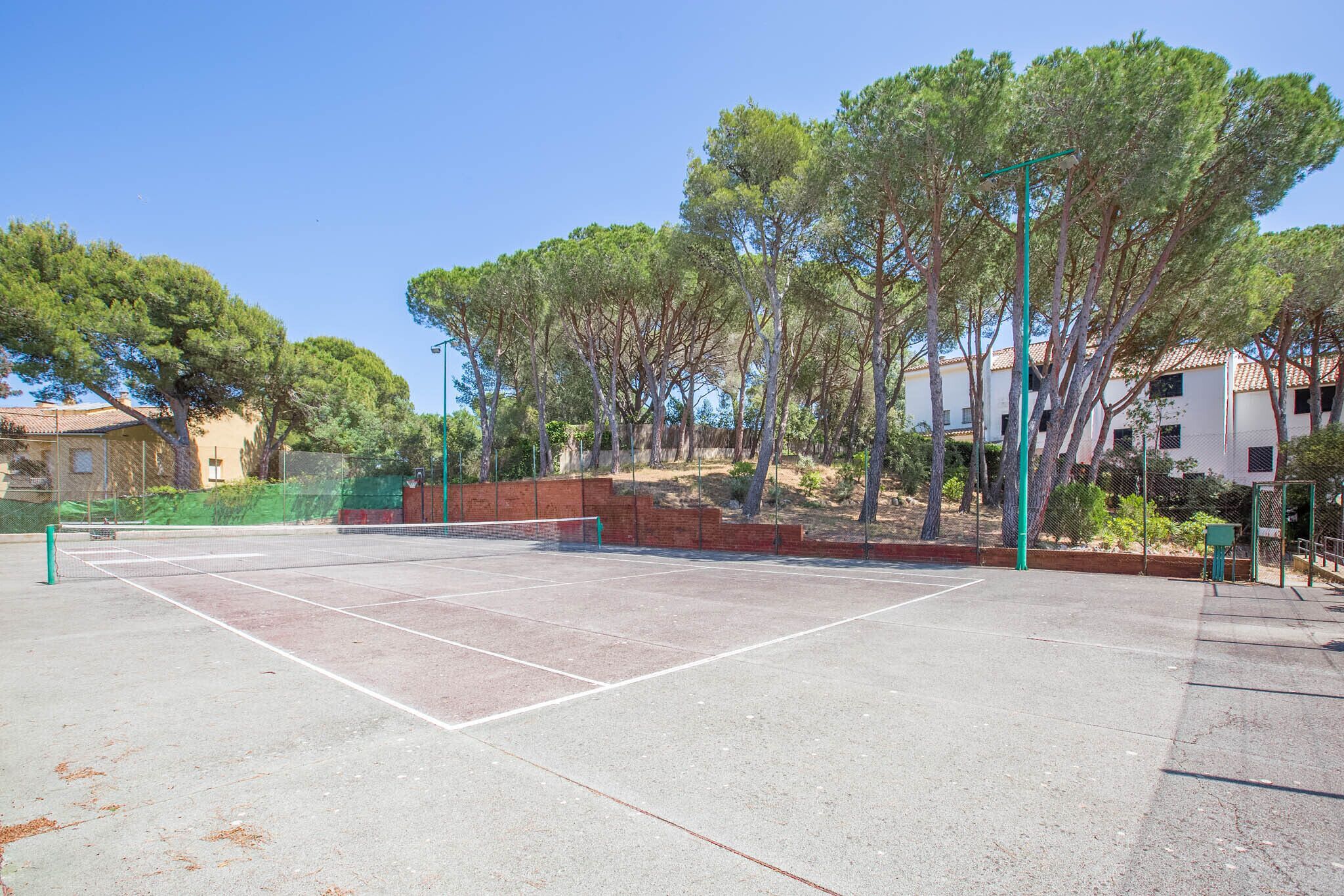 Ein Tennisplatz im Freien, umgeben von Bäumen und Gebäuden.