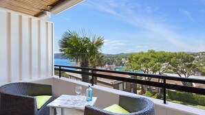 A balcony with wicker furniture, a table, and a view of a coastal town.