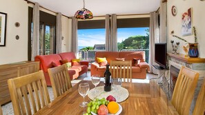 Ein geräumiges Wohnzimmer mit einem Holzesstzimmerstisch, roten Sofas und einem Balkon mit Aussicht.