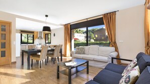 Un salon moderne comprenant un canapé, une table basse, un coin repas avec des chaises et une grande fenêtre avec des rideaux.