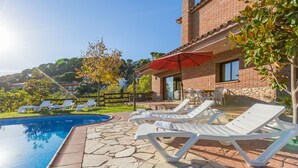 Un espace piscine avec des chaises longues et un parasol rouge, entouré d’un bâtiment en briques et de verdure.