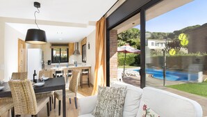 Une cuisine moderne avec un coin repas, une grande fenêtre donnant sur une piscine et un jardin.