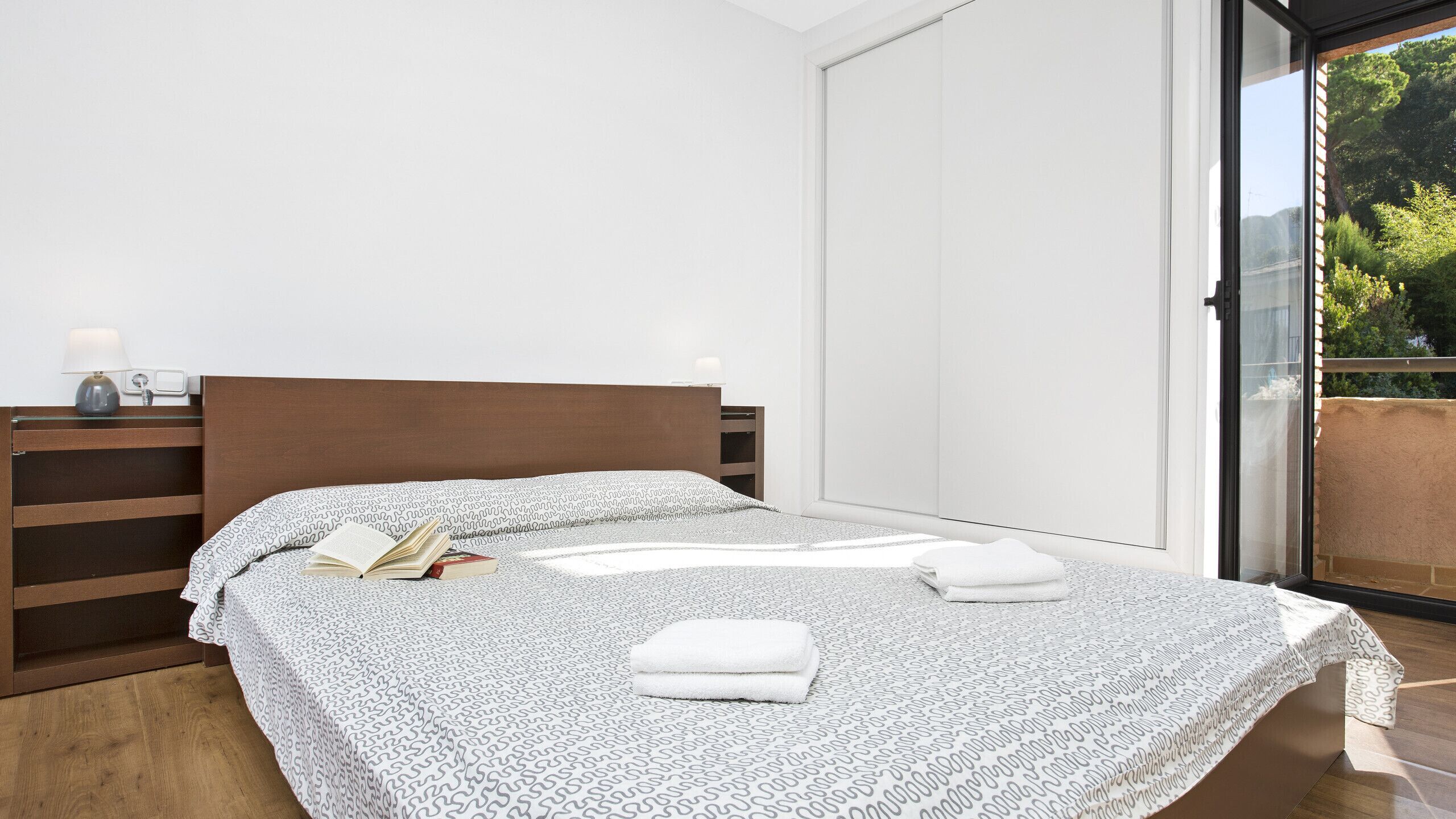 Ein modernes Schlafzimmer mit einem Holzkopfende, einer gemusterten Bettdecke und einem Nachttisch mit einer Lampe.