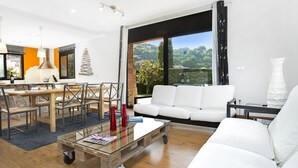 A spacious living room with a large window, a white sofa, a glass coffee table, and a dining area with a wooden table and chairs. - 2PON01 - Beautiful house with private pool located in a quiet area near the beach (Lloret de Mar)