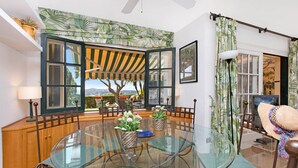 A dining area with a glass table, wicker chairs, and a view of a tree and landscape through open windows. - 1SB 28 - Nice and comfortable 150m2  house with communal pool located in Llafranc, 500m from the beach (Llafranc)