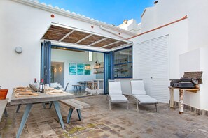 Un amplio patio con una mesa de comedor para cuatro, sillas exteriores y una estación de parilla.