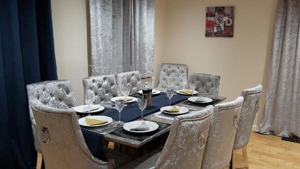 Uma sala de jantar com uma mesa retangular posta para seis pessoas, cadeiras estofadas e um quadro na parede.